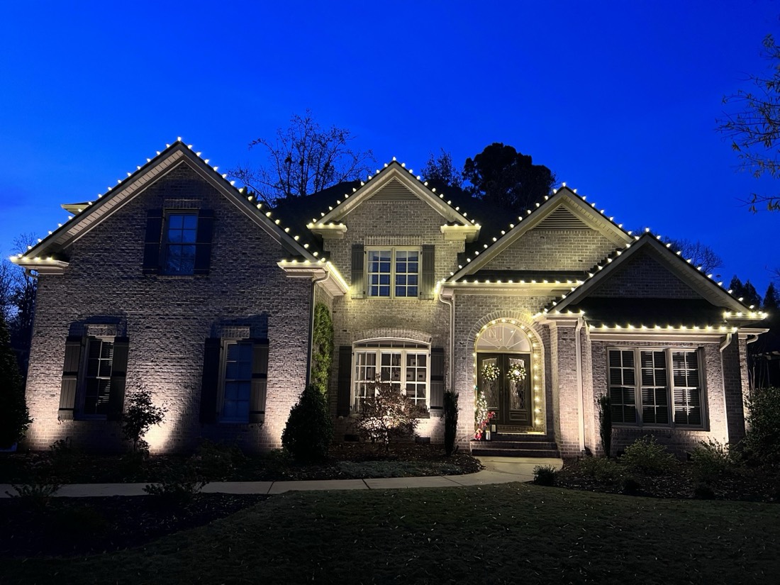 A home's roofline lit with warm white Christmas lights at twilight